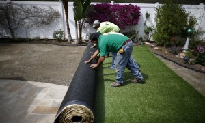 rolling-out-artificial-grass-in-yard-300x180