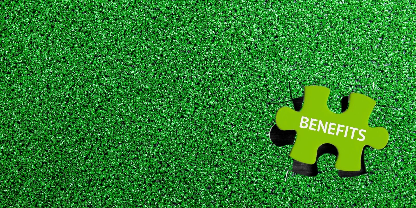 Green puzzle piece labeled 'Benefits' placed on vibrant artificial grass surface, symbolizing the advantages of synthetic turf. Green artificial turf background with a puzzle piece