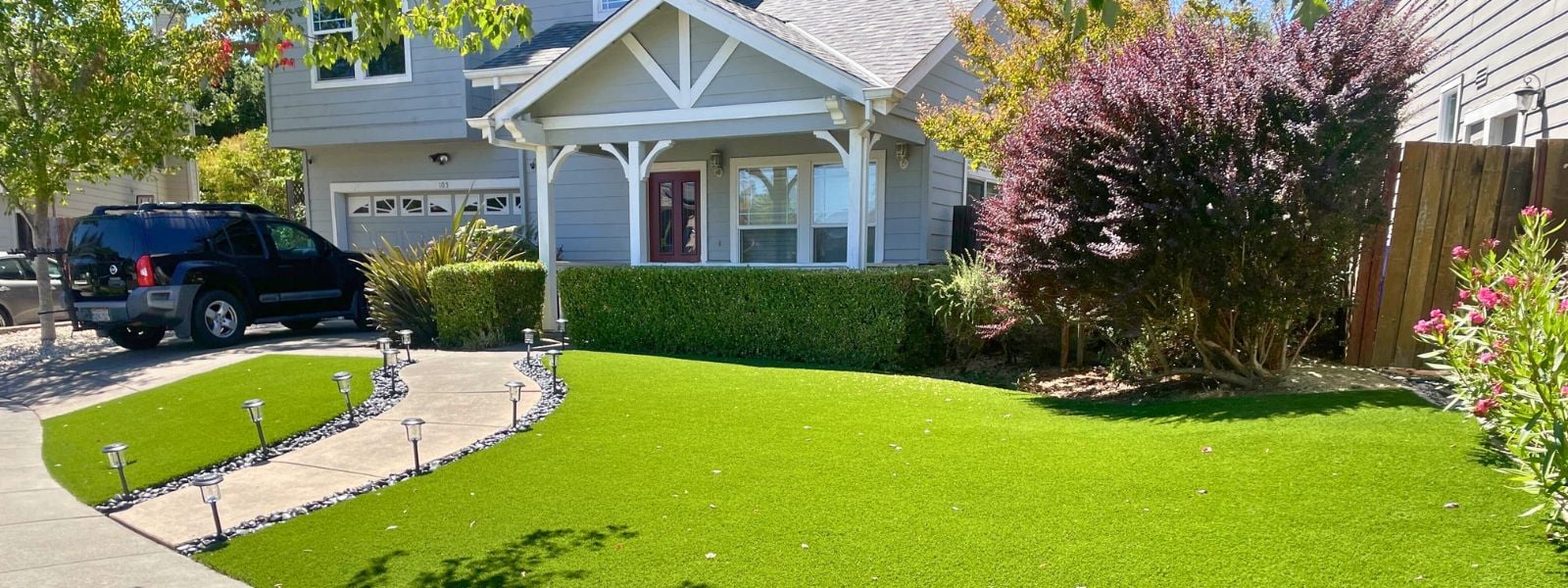 Front yard of a suburban home with neatly installed artificial grass lawn, decorative pathway lights, and vibrant landscaping. Lush green artificial turf lawn enhancing curb appeal in San José